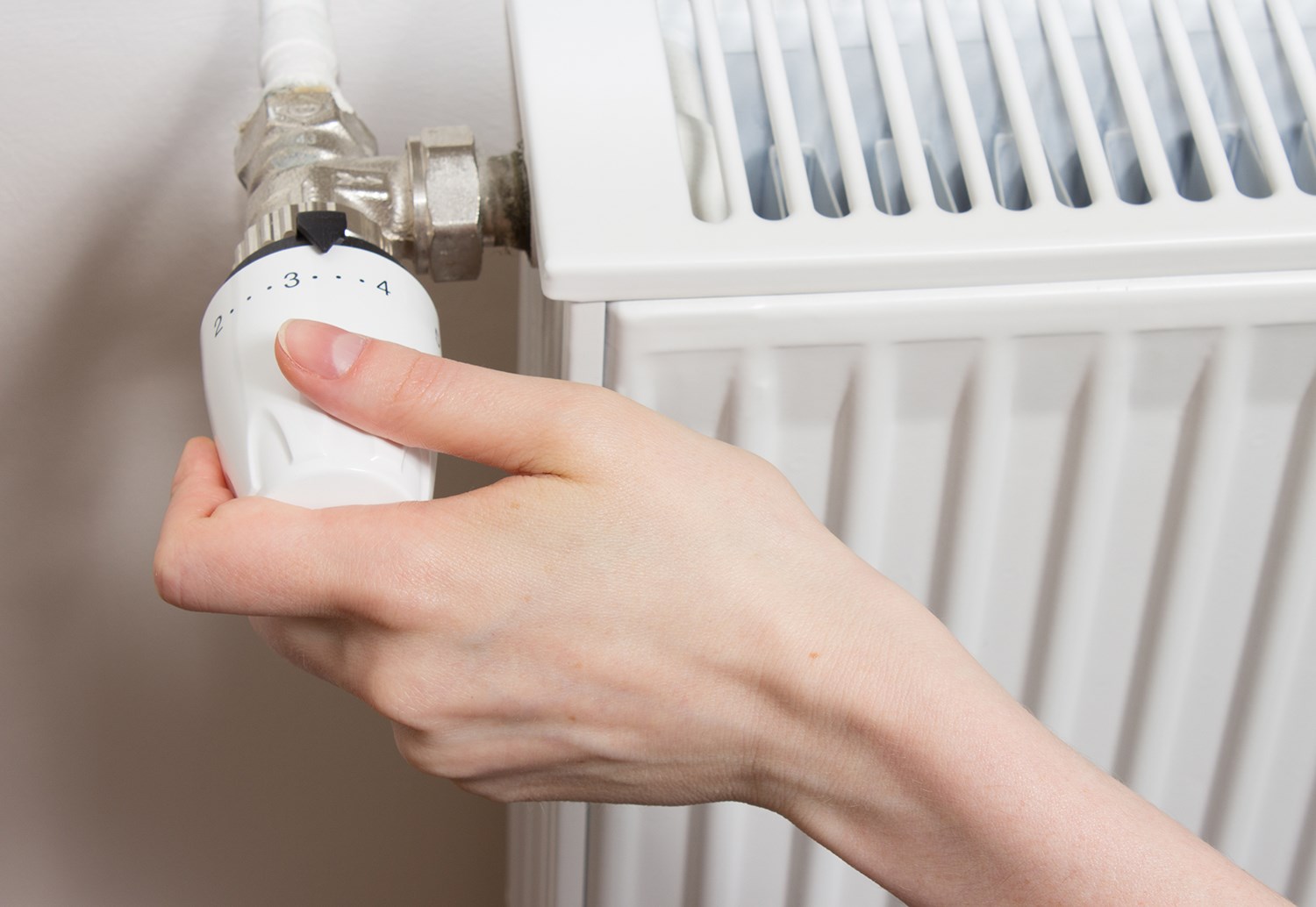 En person som skruvar på termostaten på ett element. 