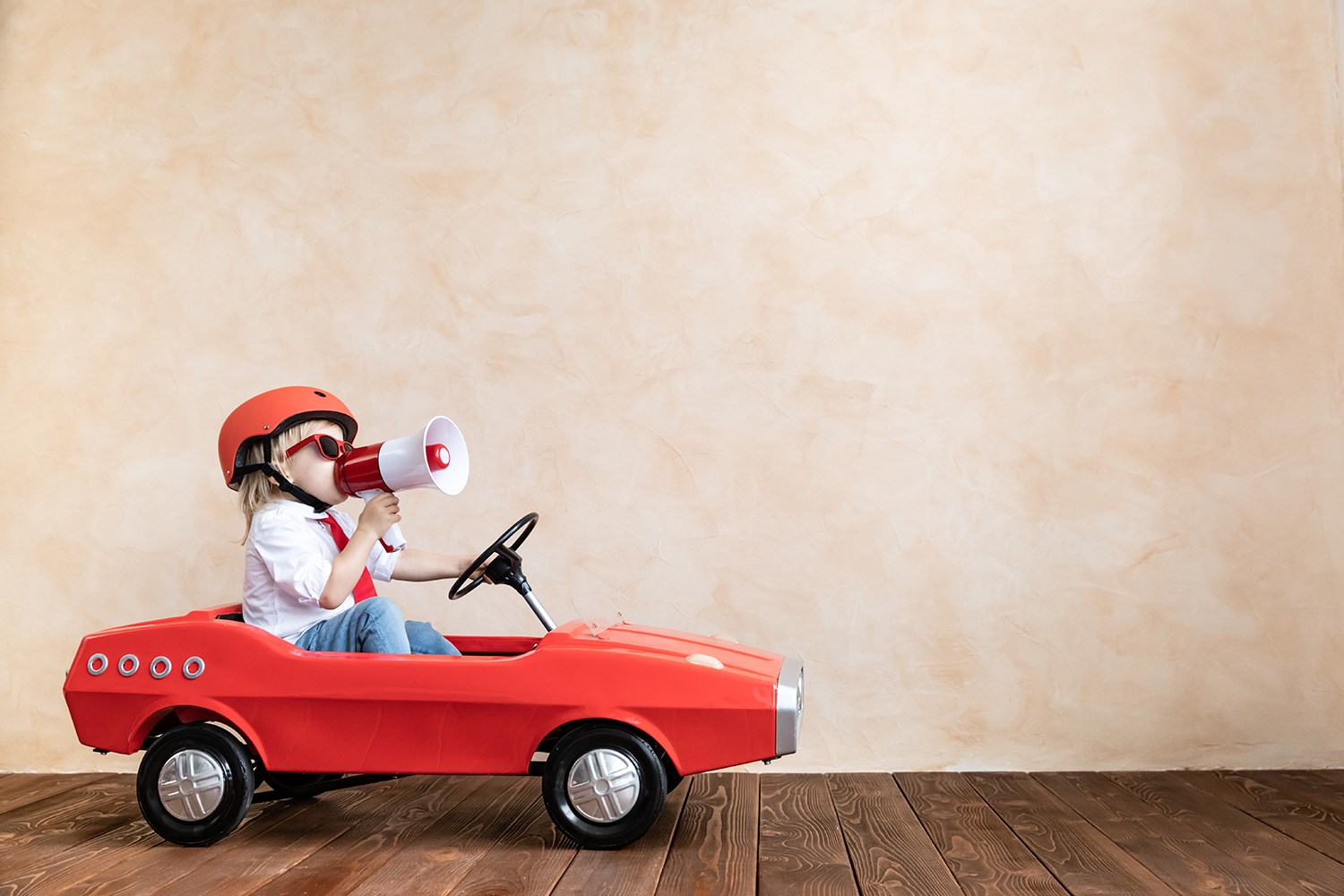 Barn som sitter i en liten röd barnbil, med hjälm och en mikrofon.
